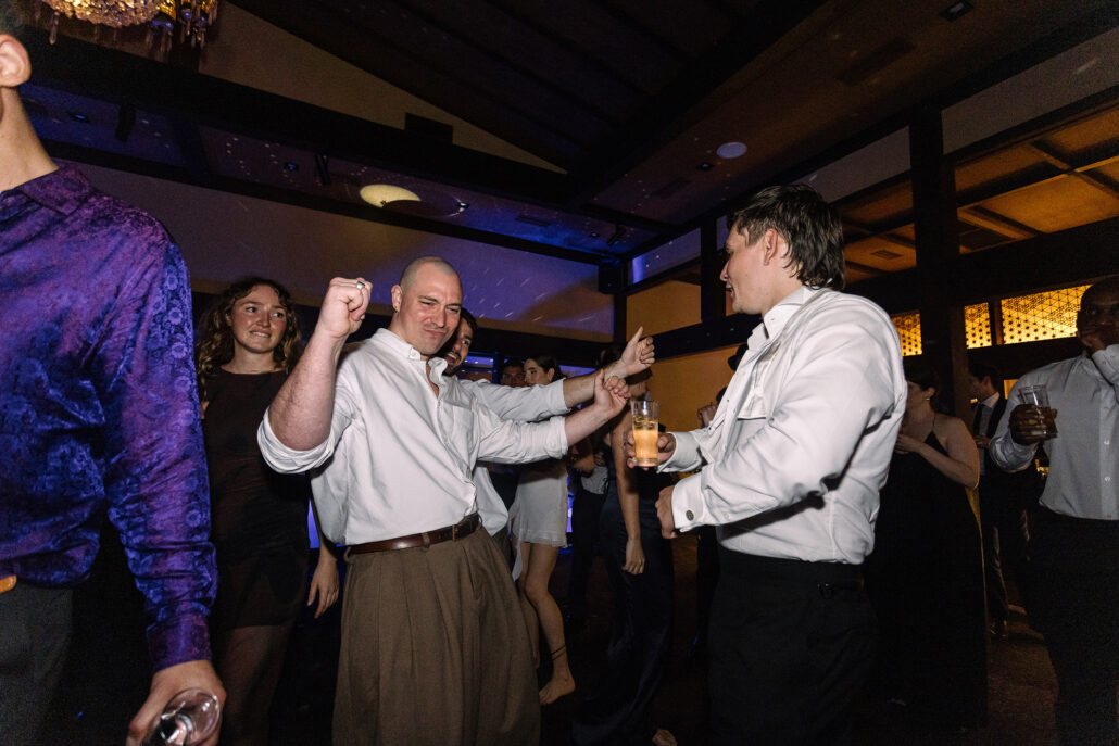 Guests dance together, one in a purple shirt, late in the night.
