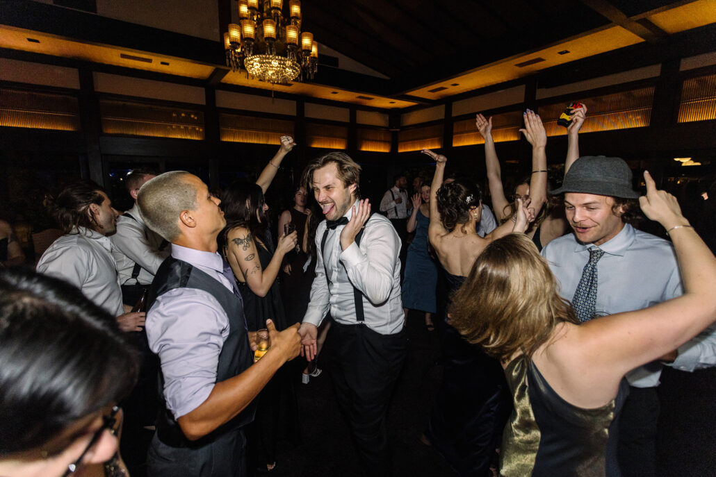 Guests dance with their hands up under the chandelier.