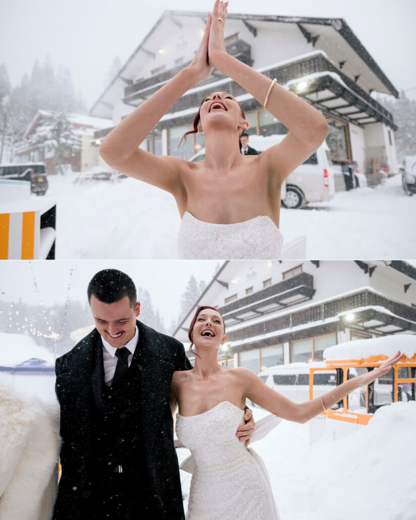 The bride throws her arms up in the falling snow outside a snow covered lodge, and the groom laughs beside her as they arrive for apres ski in Hakuba.