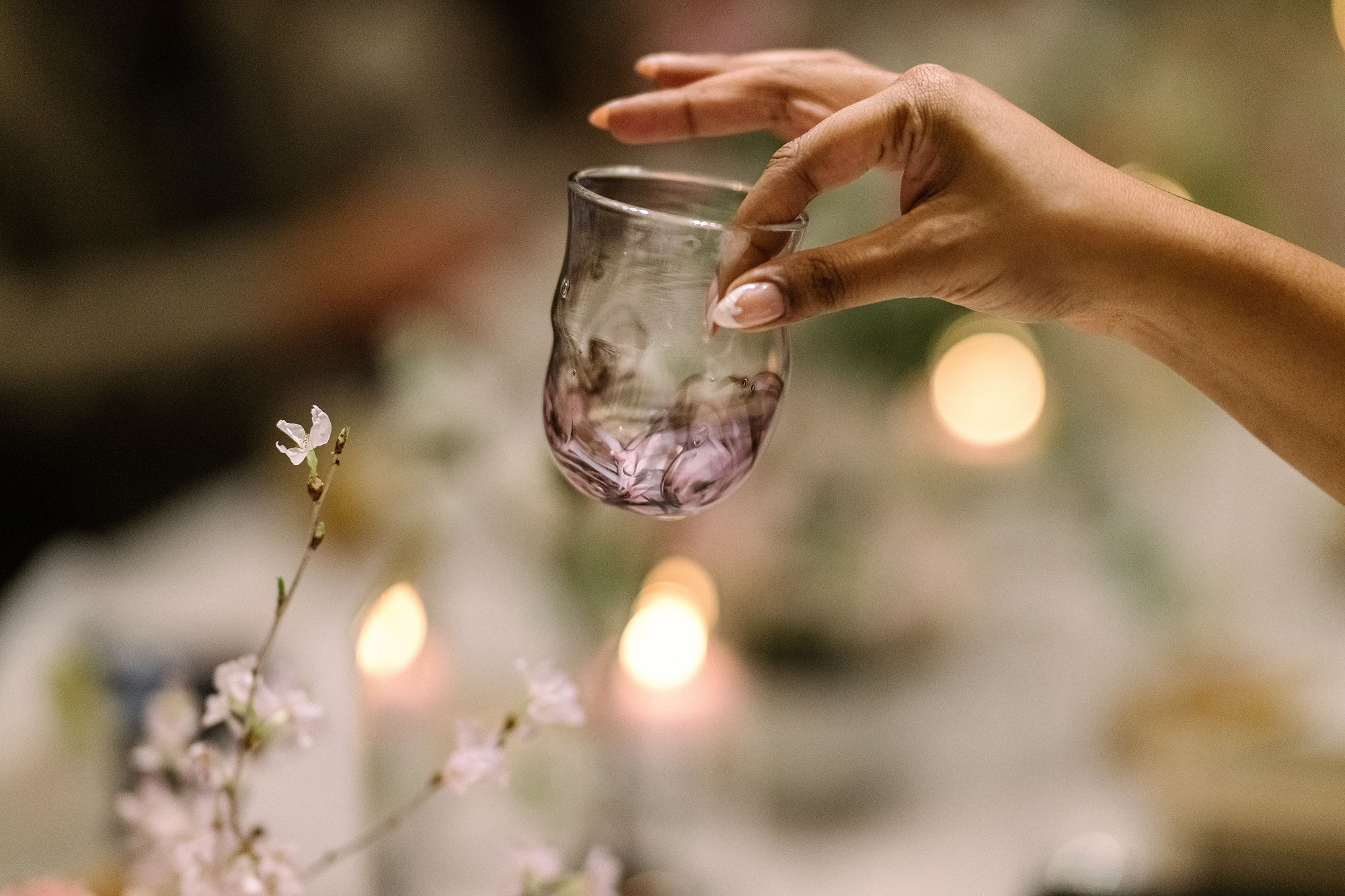 A guest lifts a pink glass cup, a gift waiting at every place, above blossom and candlelight at a ryokan wedding reception in Japan.