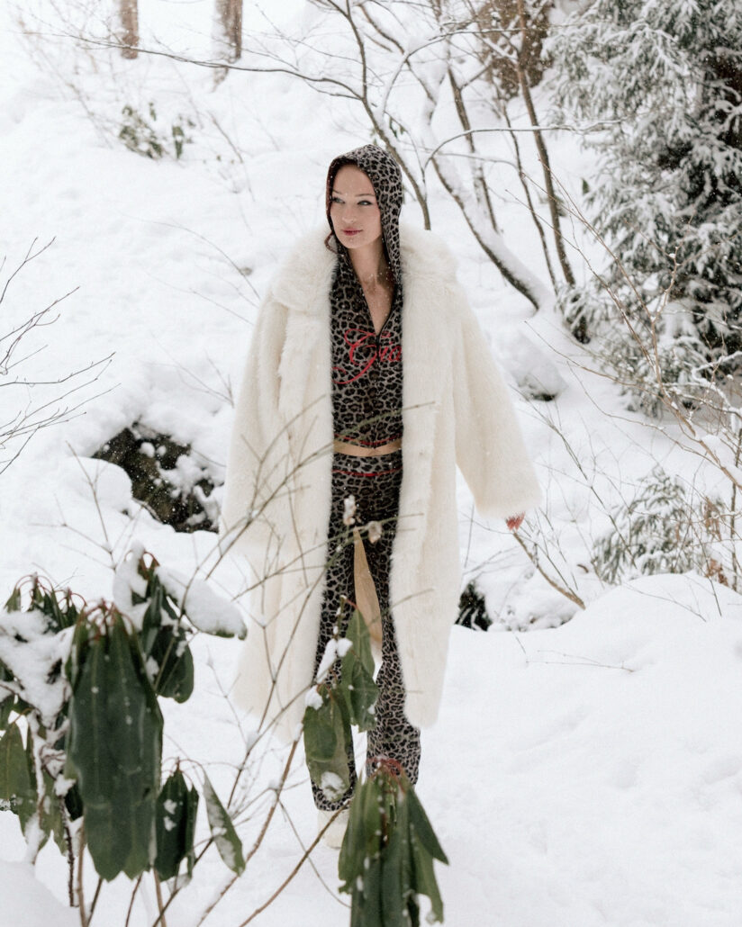The bride in a white faux fur coat and leopard print walks through deep snow on the morning of her winter wedding in Hakuba, Japan.