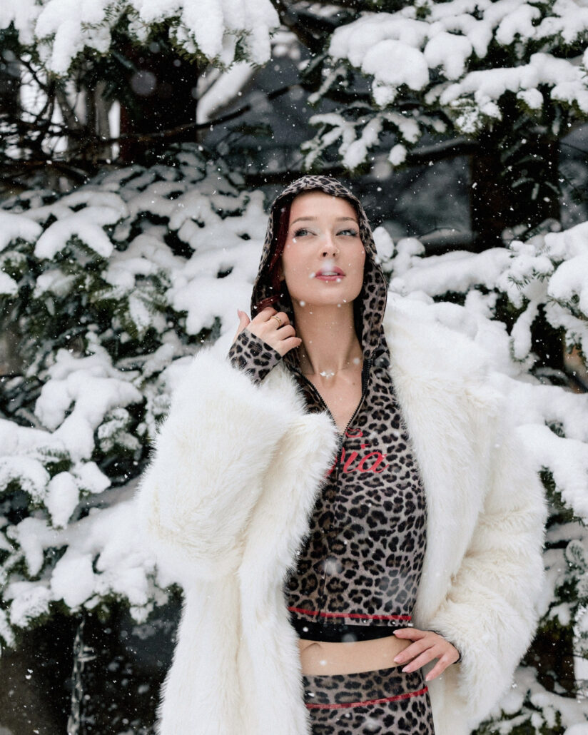 The bride laughs as snow falls on her leopard print hood and white faux fur coat among the snow covered trees in Hakuba.