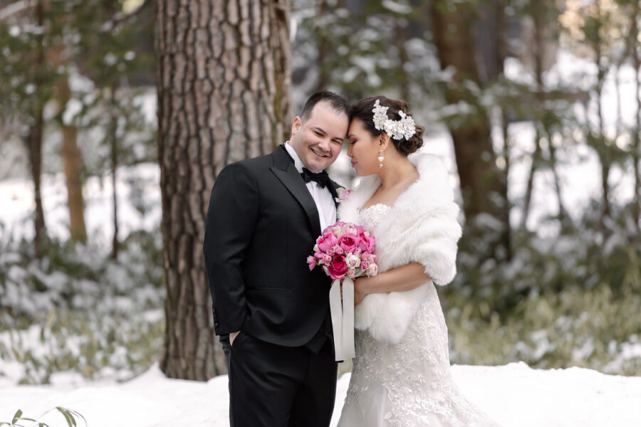 The bride and groom stand close among tall pines and fresh snow at their ANELLI Karuizawa wedding.
