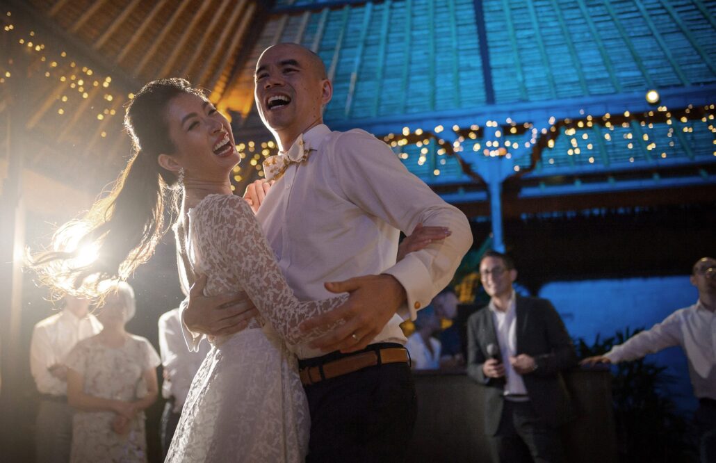 The bride and groom laugh as they dance under strings of lights at their wedding in Ubud, Bali.