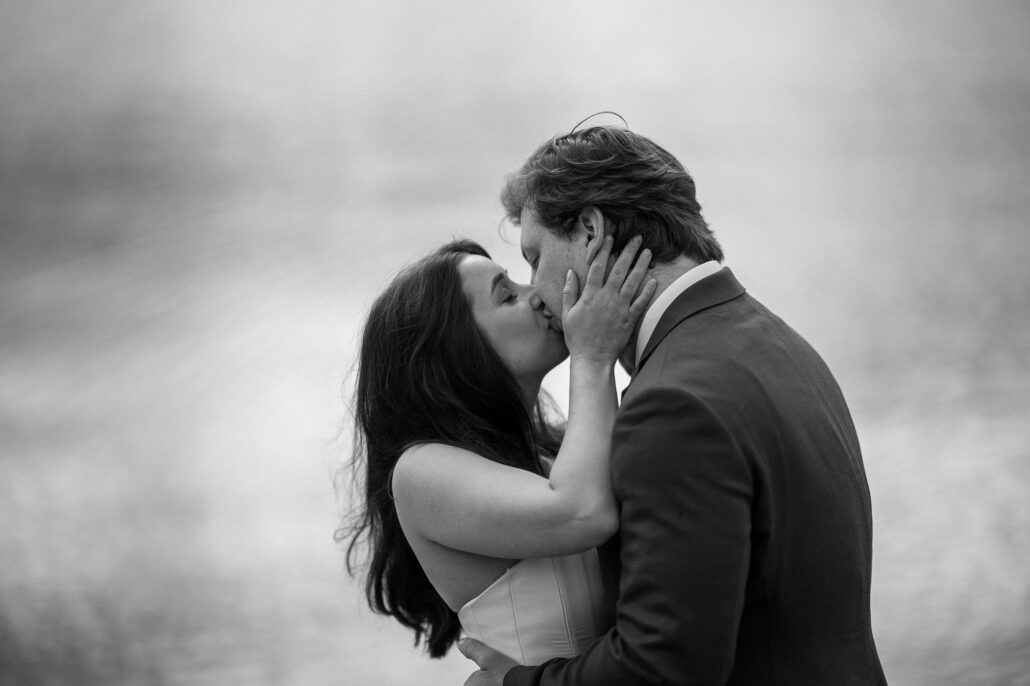 In black and white, the bride holds the groom's face as they kiss beside the water, a moment from a Lake Kawaguchiko elopement.