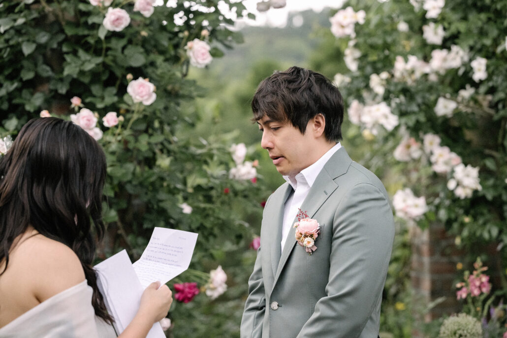 The bride reads to the groom from a handwritten page among climbing roses in a garden in Atami.