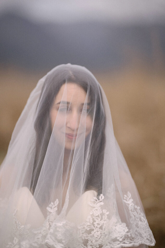 The bride looks out from beneath a long lace-edged veil against golden grass, a bridal portrait from a Mt Fuji elopement.