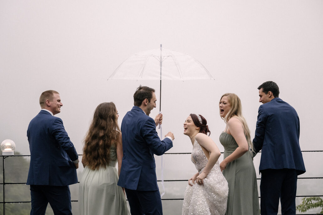 The bride laughs with her wedding party under a clear umbrella on a misty day near Mt Fuji.
