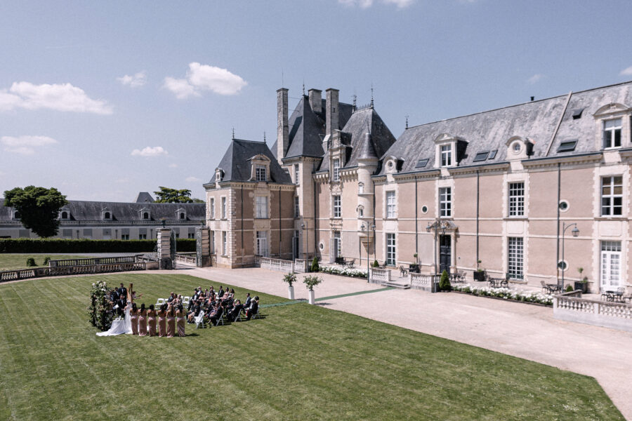 A wide view of the Château de Jalesnes wedding ceremony on the front lawn, guests seated before the château under a blue sky.