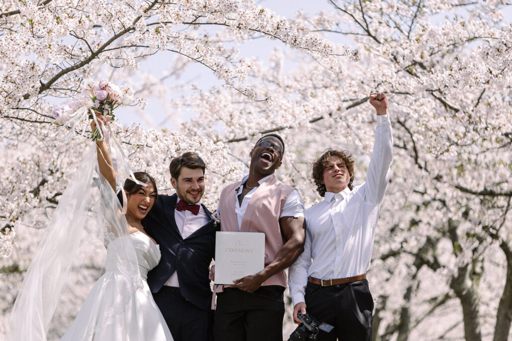 The newlyweds and their friends cheer with arms raised under the cherry blossom moments after the ceremony in Aomori.