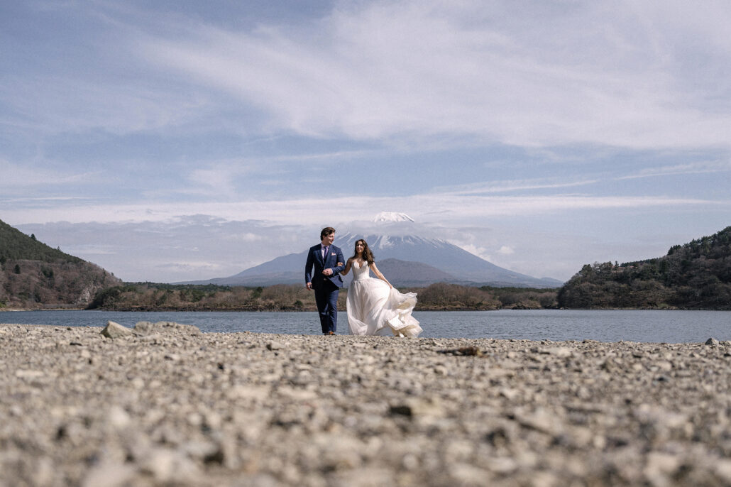 A wide view of the couple walking the stony beach at Lake Shoji with Mt Fuji in the distance, an elopement at the Fuji Five Lakes.
