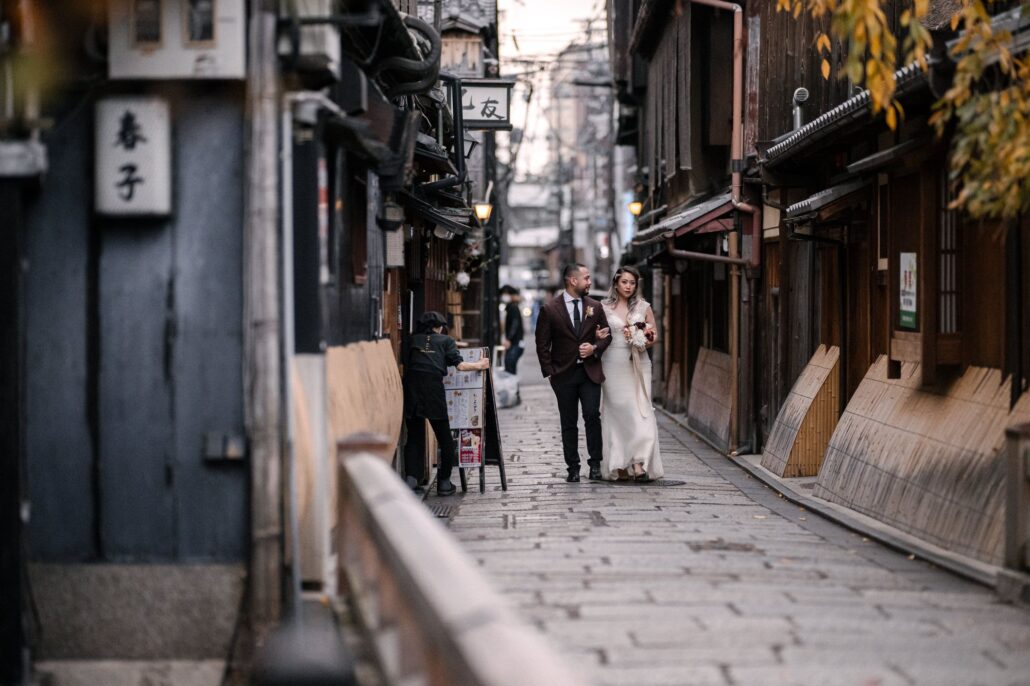The bride and groom walk down a narrow Gion lane lined with wooden townhouses.