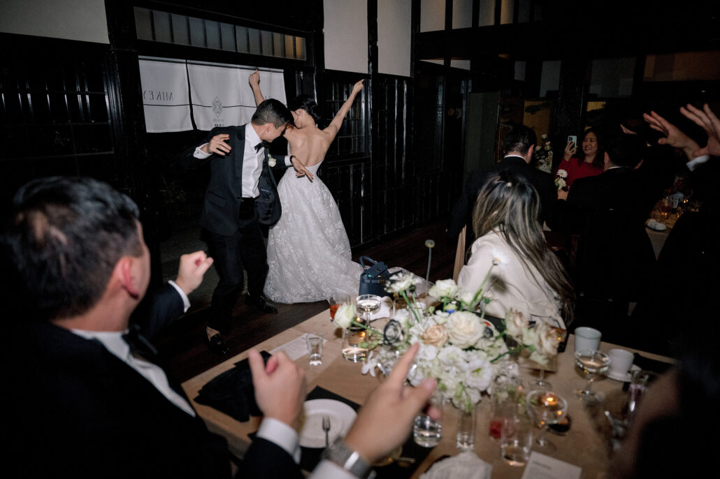 The groom spins the bride into a dip between the tables as their guests cheer them on.