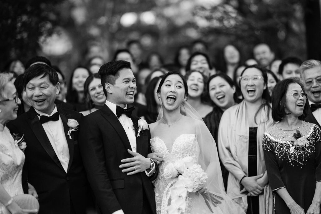 In black and white, the couple and their families laugh in the middle of the crowd as the group photo comes together.