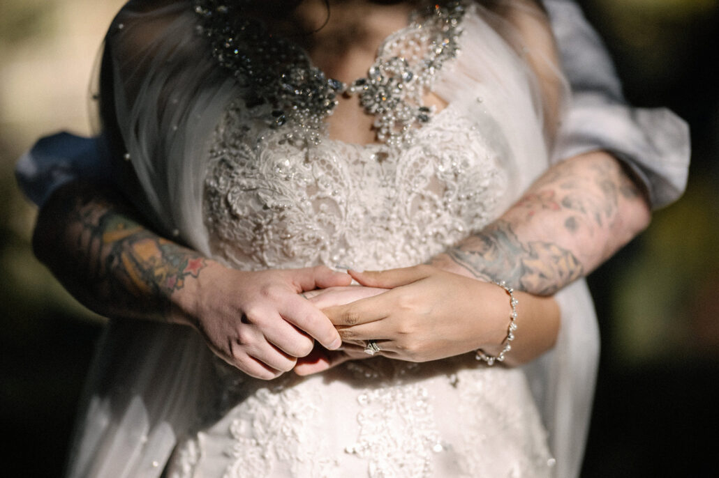 Already legally married at home, the groom's tattooed arms wrap around the bride, her ring on, against her beaded lace gown at their wedding in Tokyo, Japan.