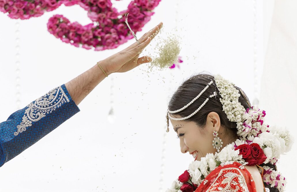 Rice is thrown over the bride in her jewelled headpiece and flower garland, a blessing at an Indian wedding in Hawaii.