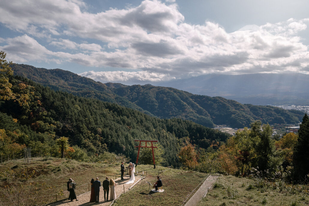 A wide view of the hillside above Lake Kawaguchi, where six guests and a cellist gather near the red torii for an intimate wedding in Japan.