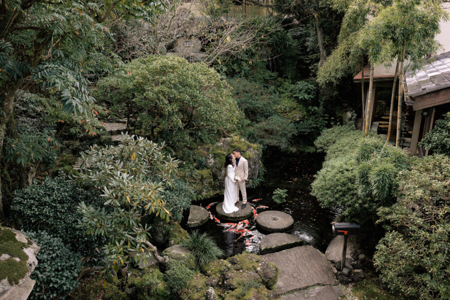 The couple kiss on a round stepping stone in the koi pond of the Japanese garden at ABBA Resort Izu, their Japan elopement venue.