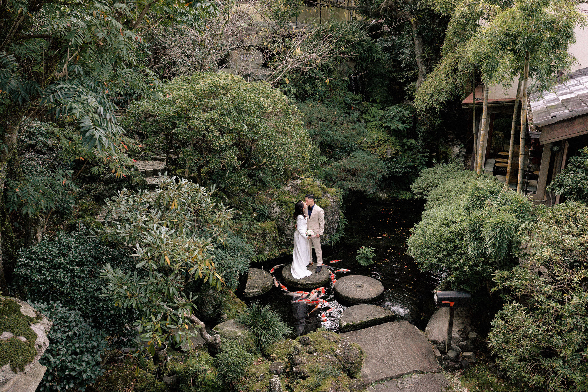 The couple kiss on a round stepping stone in the koi pond of the Japanese garden at ABBA Resort Izu, their Japan elopement venue.