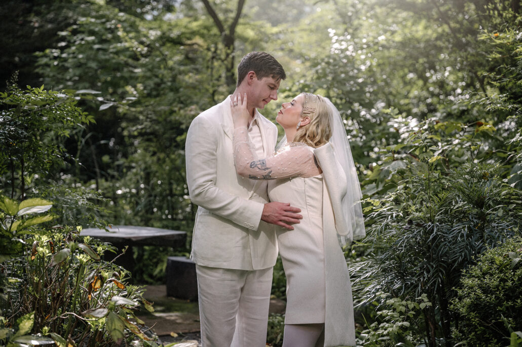 The couple hold each other in a lush Japanese garden beside a dark stone table, greenery all around their elopement portrait.