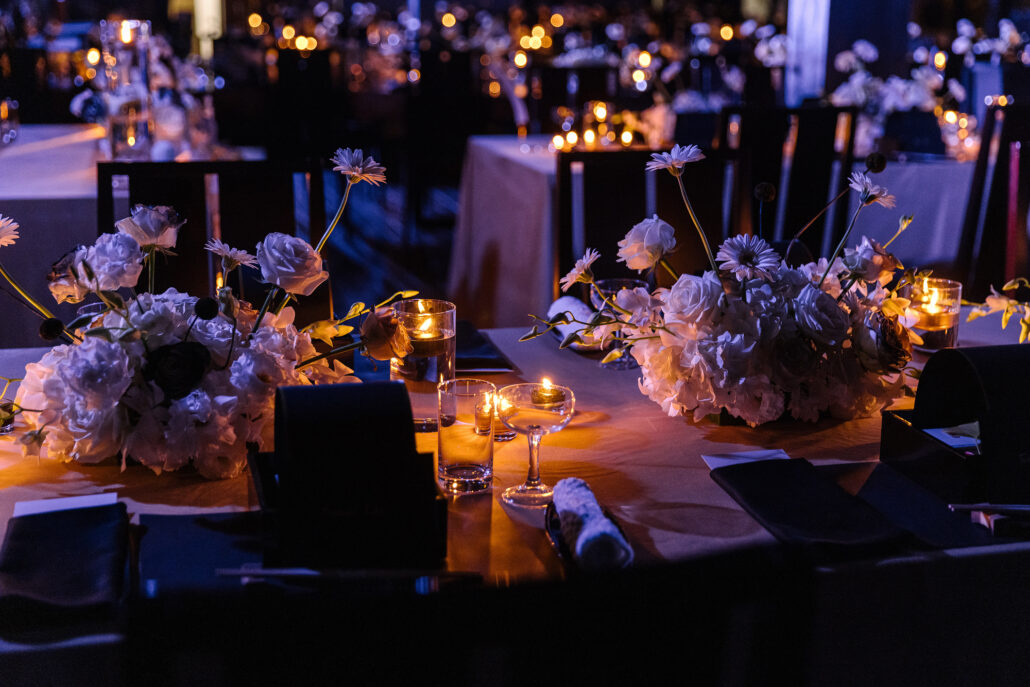 Pale flowers and candlelight along the tables of a wedding reception in a darkened room at Jinya.