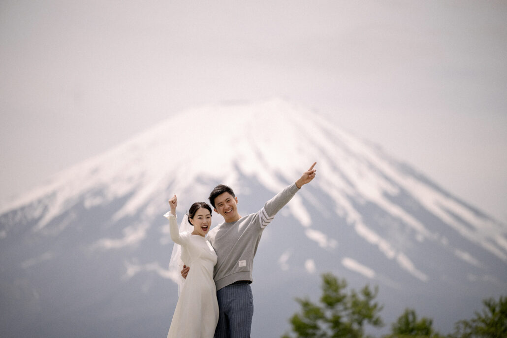 Laughing, the couple point up at the snowfields of Mt Fuji, his grey sweater and her white dress against the mountain.