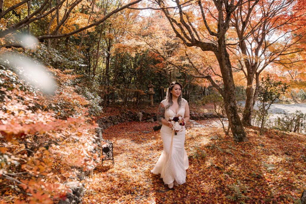 A wide view of the bride walking beneath a canopy of autumn maples in Kyoto.