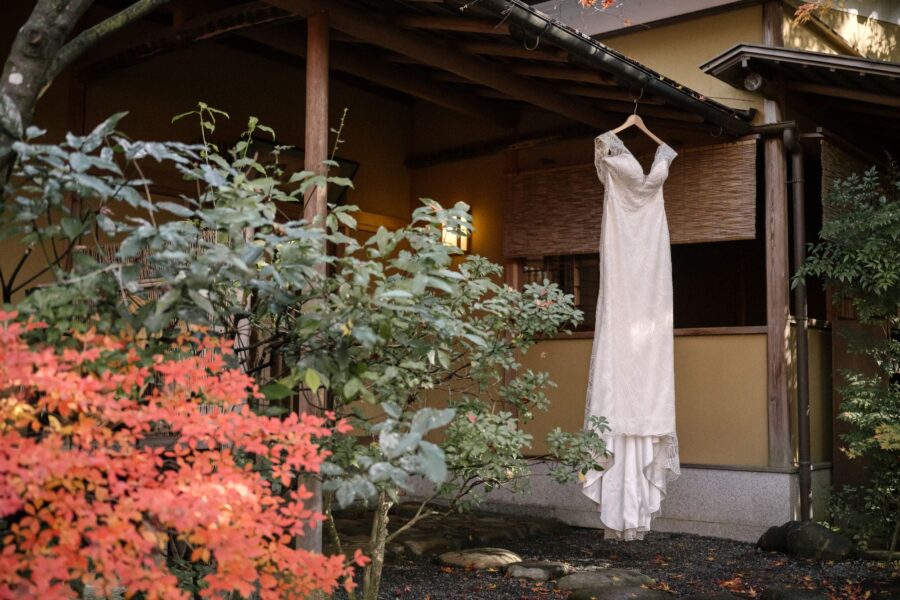 A wedding dress hangs from the eaves of a garden building among red maples on the morning of an intimate wedding in Kyoto.