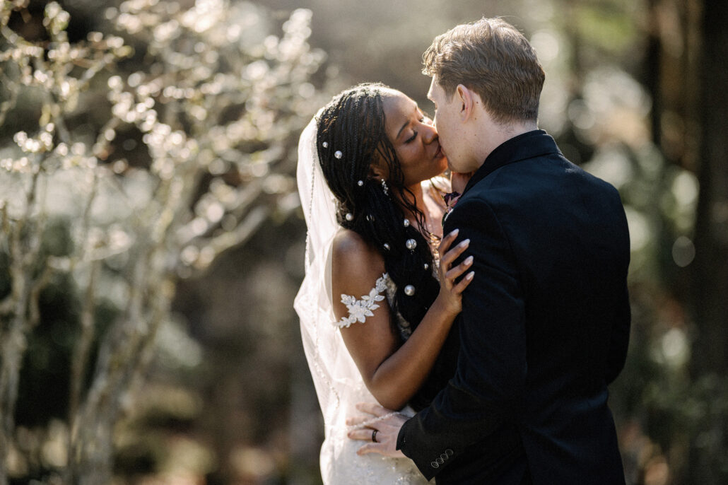 The groom kisses the bride in soft sunlight on their wedding morning in a private garden in Kyoto.