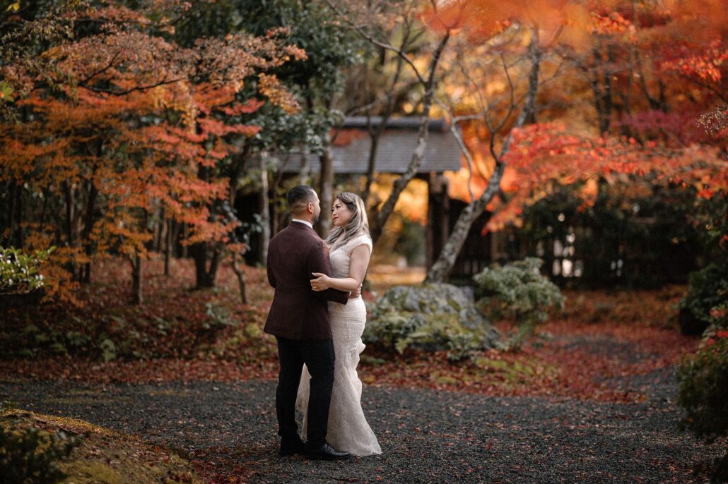 The bride and groom embrace on a garden path surrounded by autumn colour.