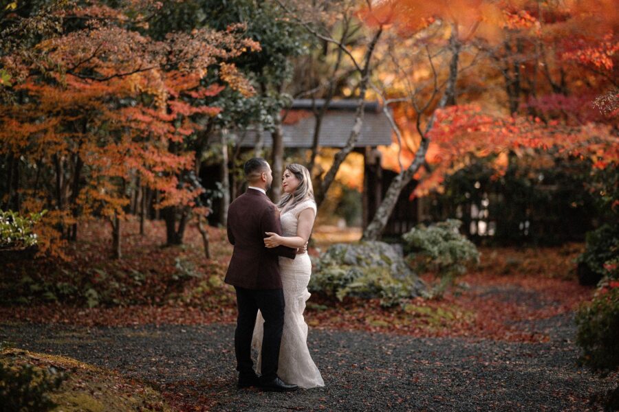 The bride and groom embrace on a garden path surrounded by autumn colour.