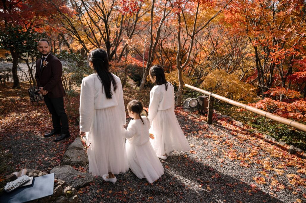 The girls stand near their father as he waits under the maples for the bride.
