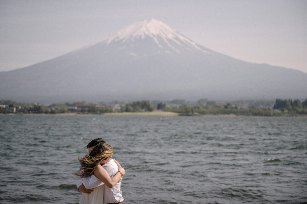 Small against the choppy water, the couple embraces on the shore of Lake Kawaguchi, Mt Fuji clear in the spring sky beyond.