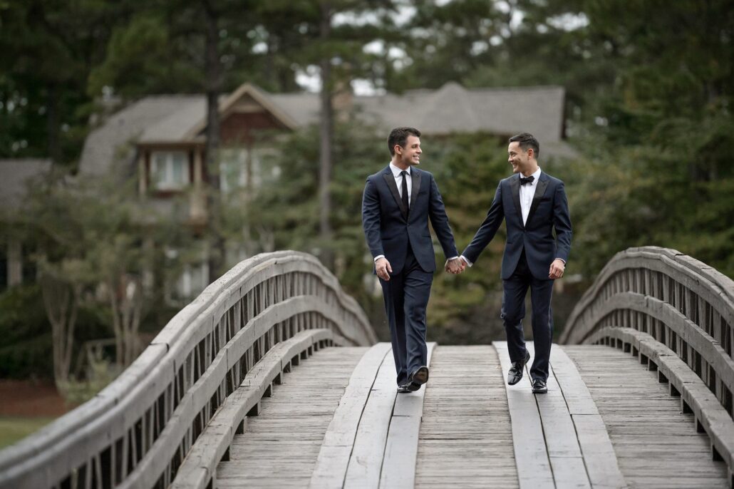 Two grooms walk hand in hand across a wooden bridge at the Ritz-Carlton Reynolds on Lake Oconee, Georgia.