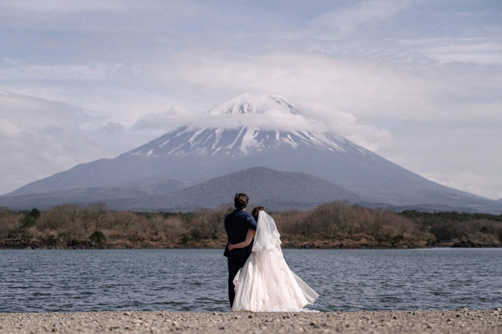 The groom and bride embrace on the shore of Lake Shoji with snow-capped Mt Fuji rising behind, a Fuji Five Lakes elopement.