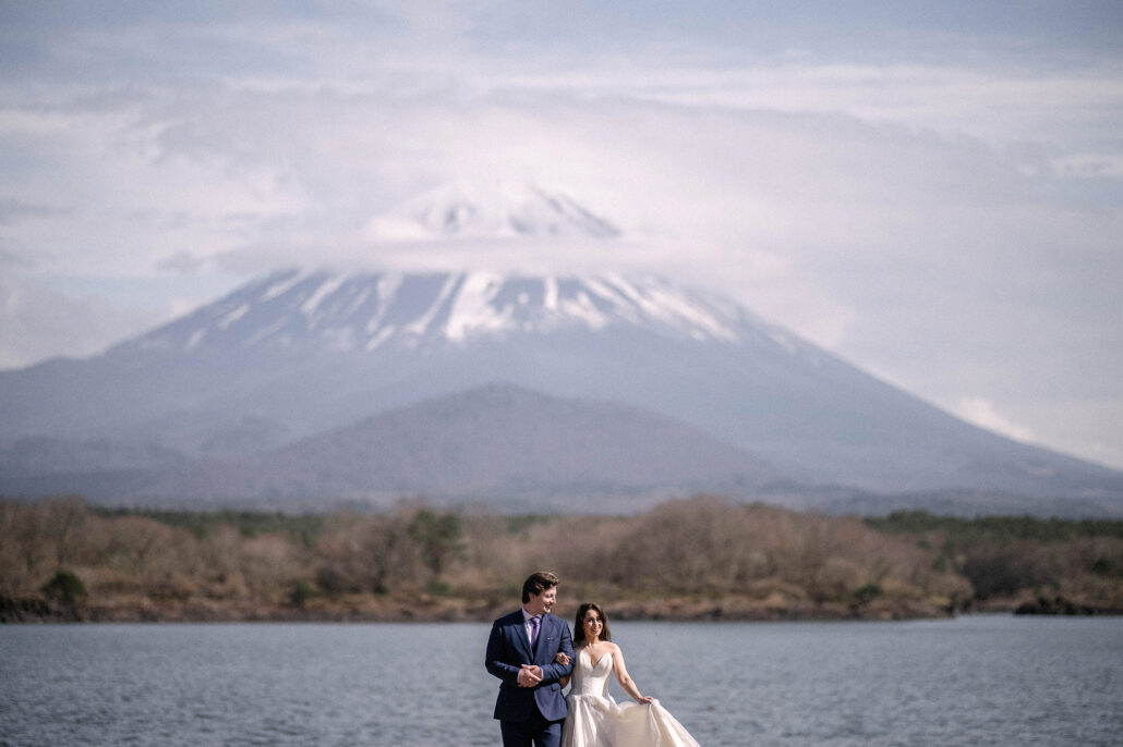 The bride and groom walk toward the camera at the edge of Lake Shoji, a ring of cloud on Mt Fuji above, a Mt Fuji elopement.