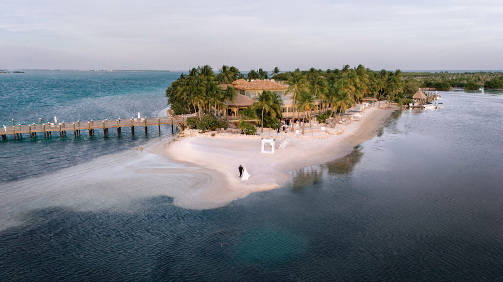 From the air, a couple stand on a sandbar curving out from Little Palm Island into the clear water of the Florida Keys.