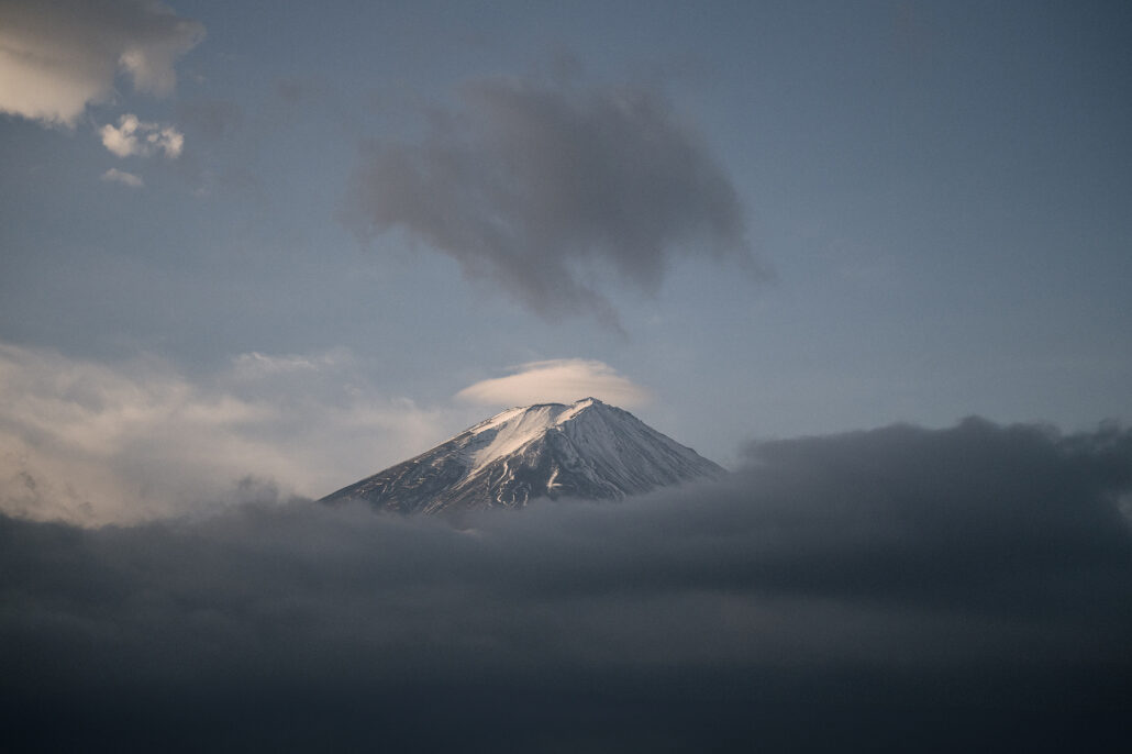 The snowy summit of Mt Fuji breaks through a bank of dark storm cloud at dawn.