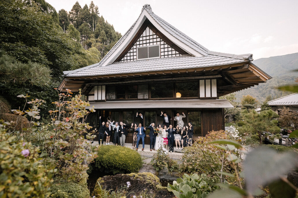 The wedding party waves from the entrance of a grand old wooden house turned village hotel in the mountains of Japan.