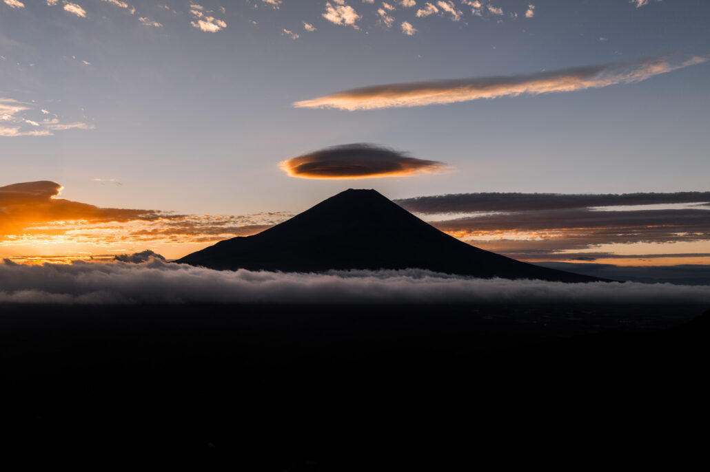 Mt Fuji in silhouette at sunrise on an elopement morning, a lens-shaped cloud resting above the summit and a sea of cloud along its base.