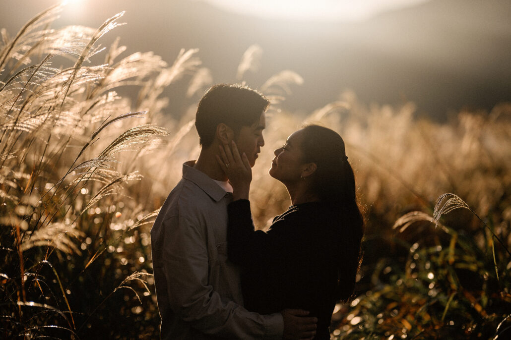 She rests her hand on his cheek as they stand in backlit grass, the hills behind Kawaguchiko fading into morning haze.