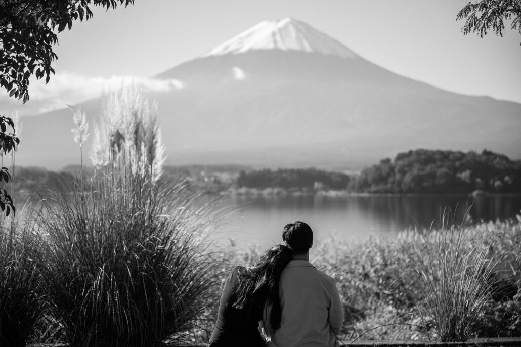 In black and white, the couple rests together beside tall pampas plumes, looking out over Lake Kawaguchi toward the cone of Mt Fuji.