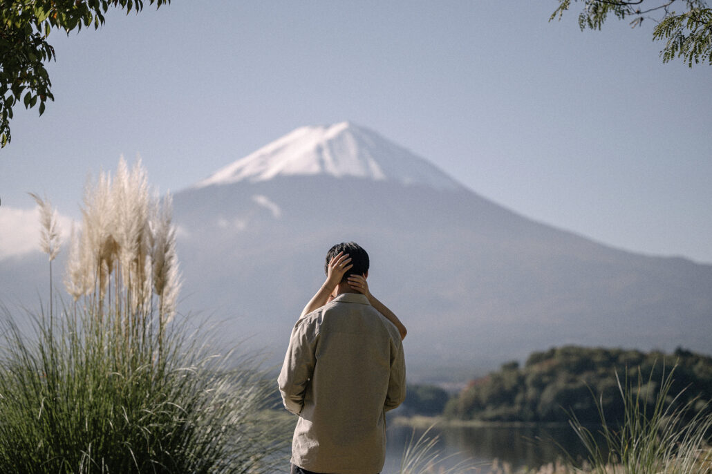 Her arms wrap around his head as they stand beside white pampas plumes, Mt Fuji and Lake Kawaguchi bright in the autumn sun.