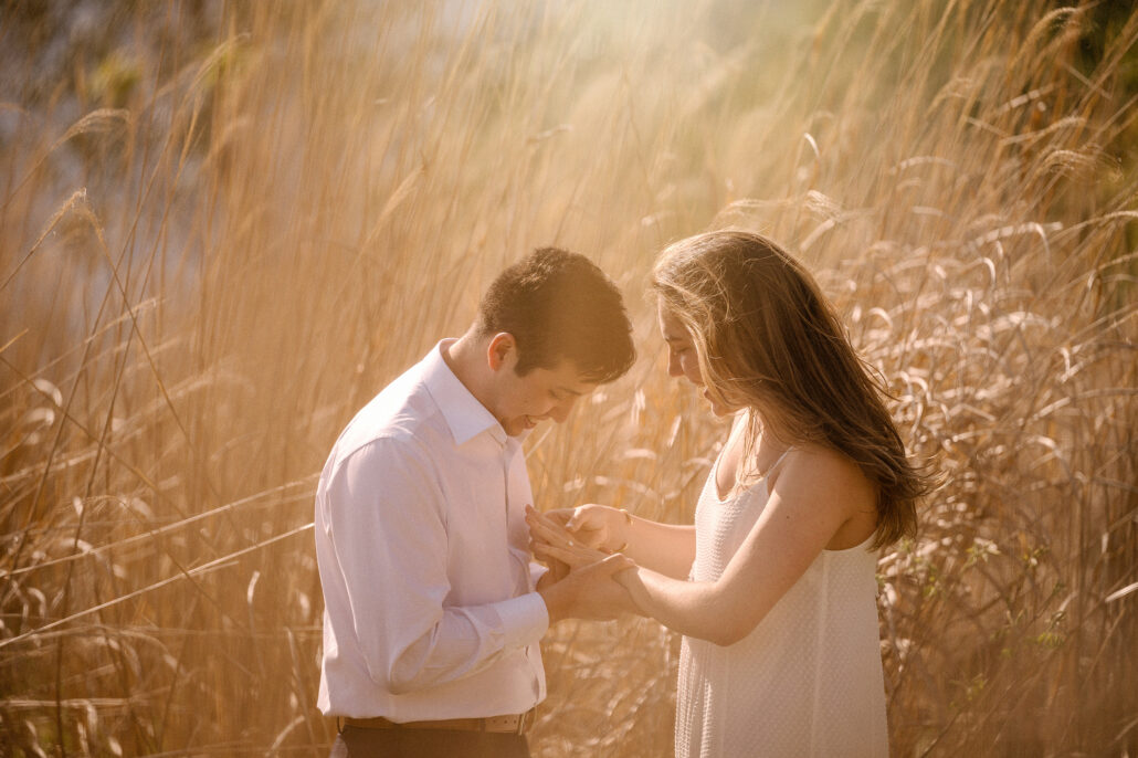In tall grass glowing gold, the couple looks down together at her hand and the new engagement ring after a Mt Fuji proposal.
