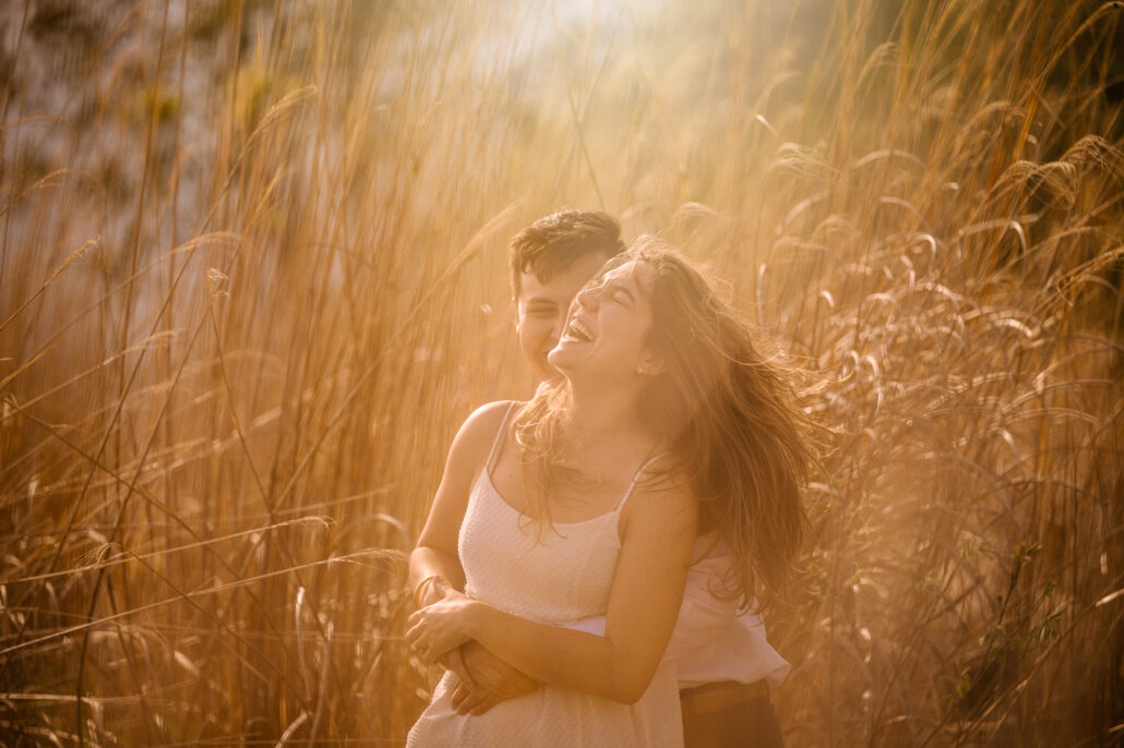 She laughs, hair blowing, as the couple embraces in tall golden grass near Lake Kawaguchi on a spring afternoon in Japan.