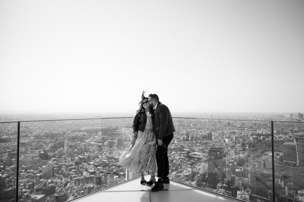 The couple kiss on the open rooftop of Shibuya Sky in black and white, Tokyo spread out to the horizon on their Shibuya elopement day.