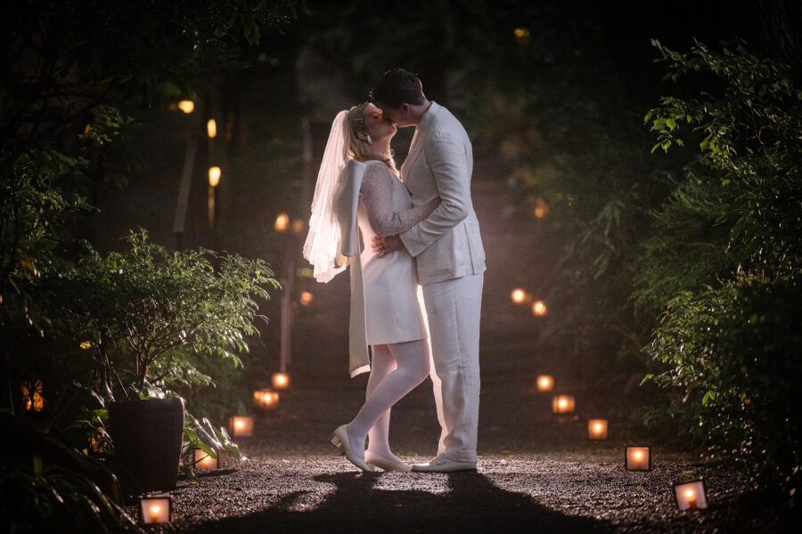 The couple kiss on a lantern-lit garden path at dusk at Jinya, a summer elopement in Japan framed by deep green leaves.