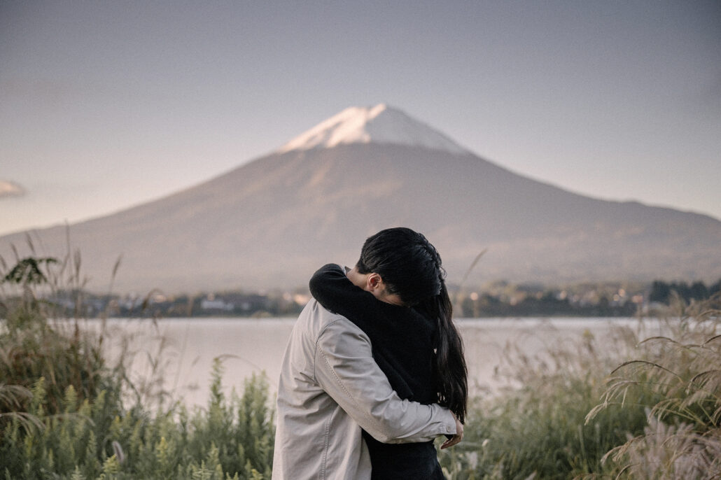 She buries her face in his shoulder in a long embrace by the lake, Mt Fuji clear and pink-tinged in the first autumn light.