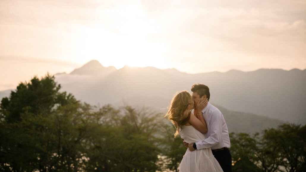 Backlit by the setting sun, the couple kisses above spring treetops near Lake Kawaguchi, the mountain ridge glowing behind.
