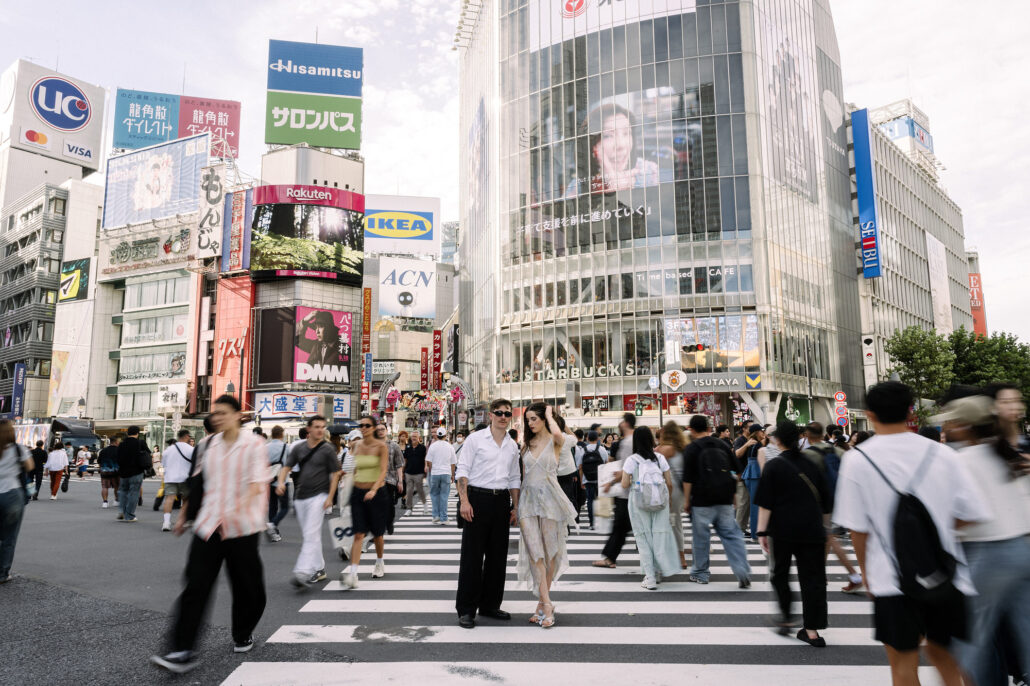 A couple walk across Shibuya Crossing in Tokyo, unnoticed among the crowds and billboards.